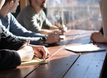 people sitting on chair in front of table while holding pens during daytime